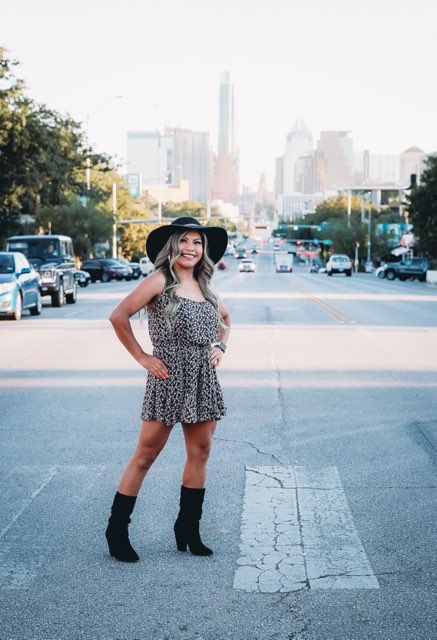 Woman with long hair smiles, hands clasped, outdoors. Background: trees, picnic tables, and people.