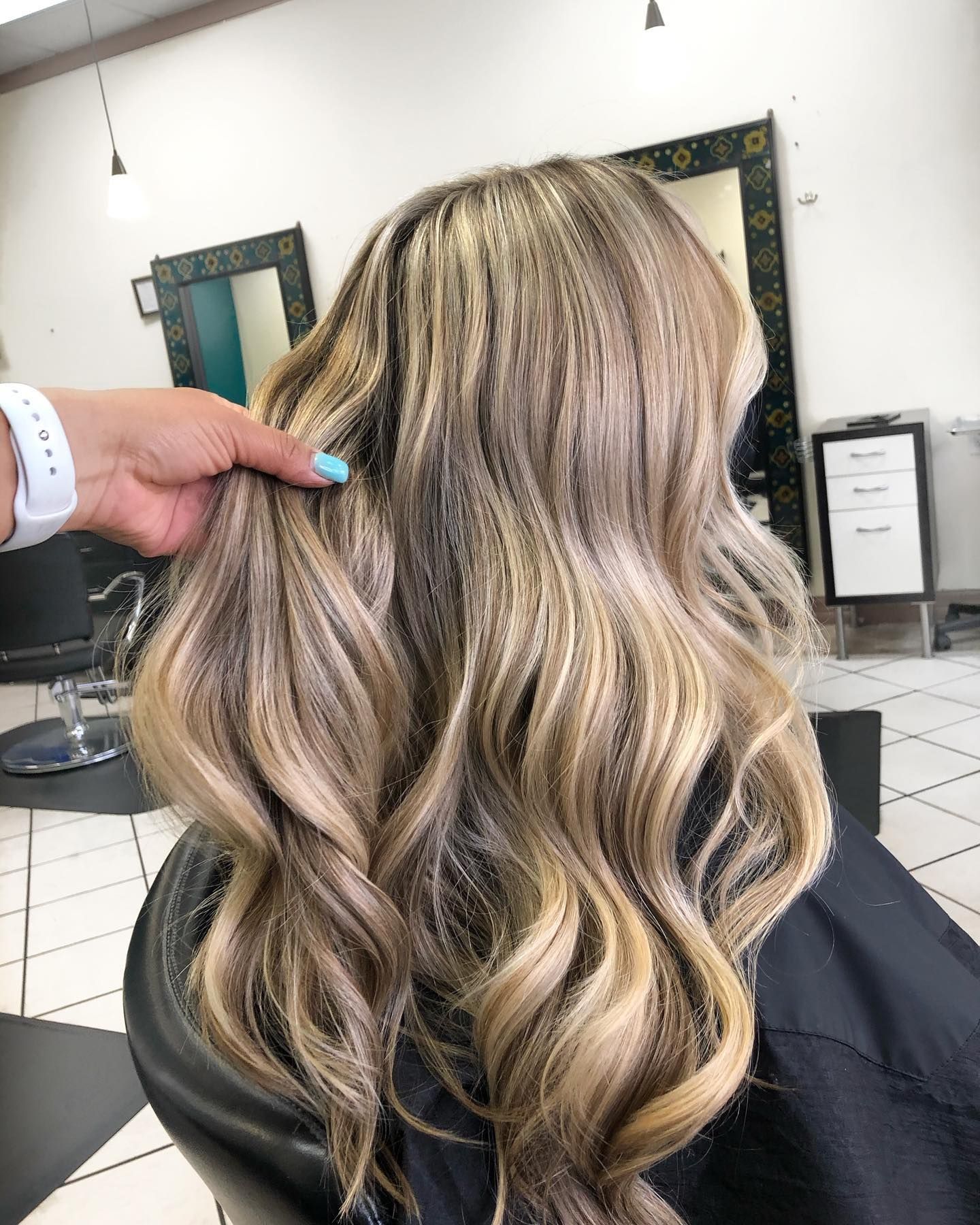 Blonde and brown wavy hair, styled in a salon, hand holding strands.