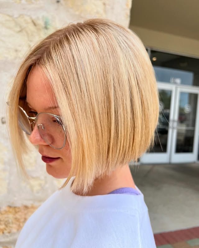 Blonde bob haircut on a woman wearing glasses, standing near a building entrance.