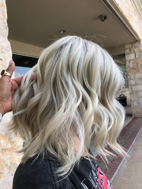Wavy, light blonde bob haircut. Hand touching hair; outdoors.