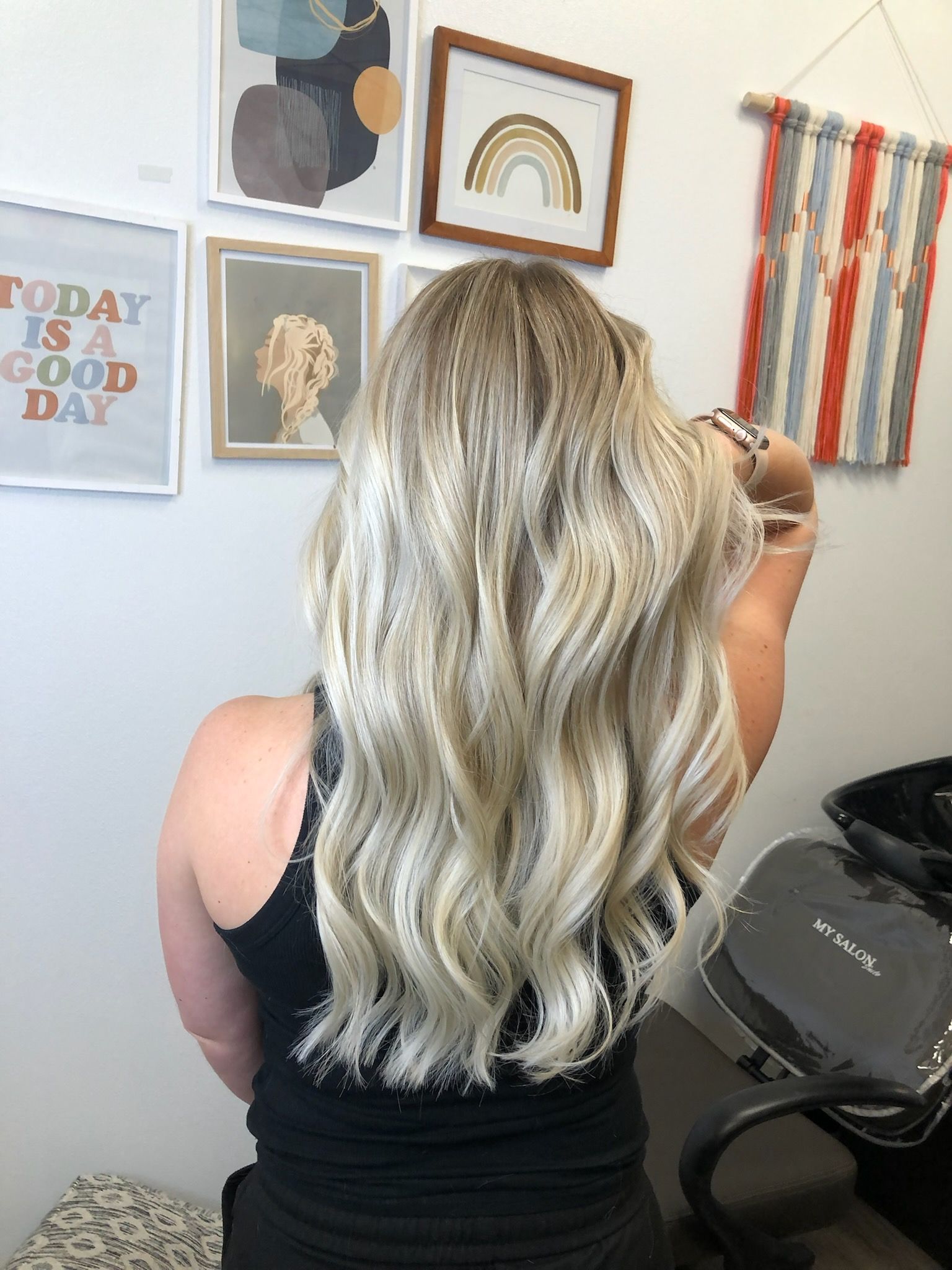 Back view of long, straight, silver-blonde hair. Person wearing a black cape, in a salon.