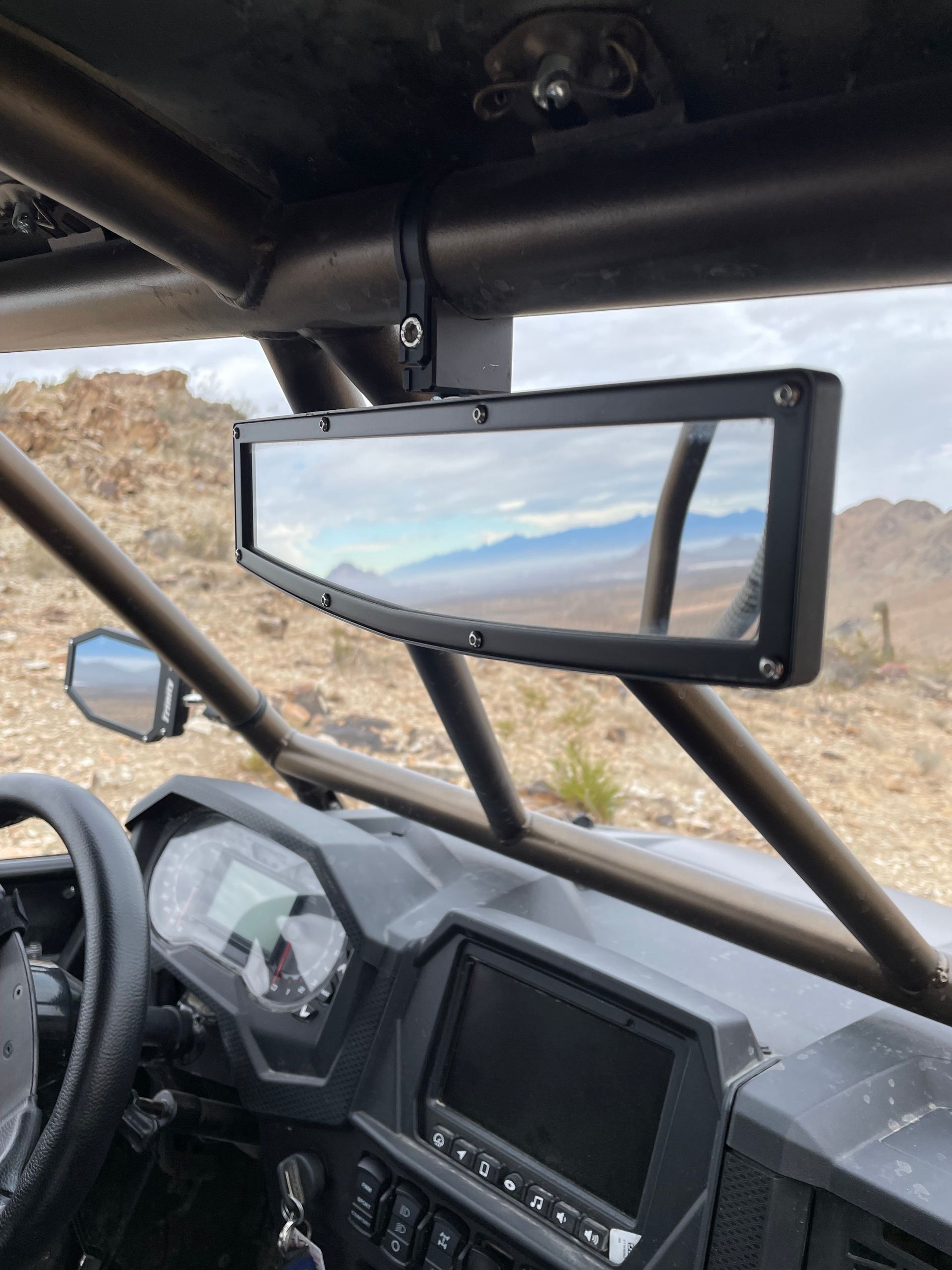 Interior view of a side-by-side UTV with a large rearview mirror showing an off-road landscape.