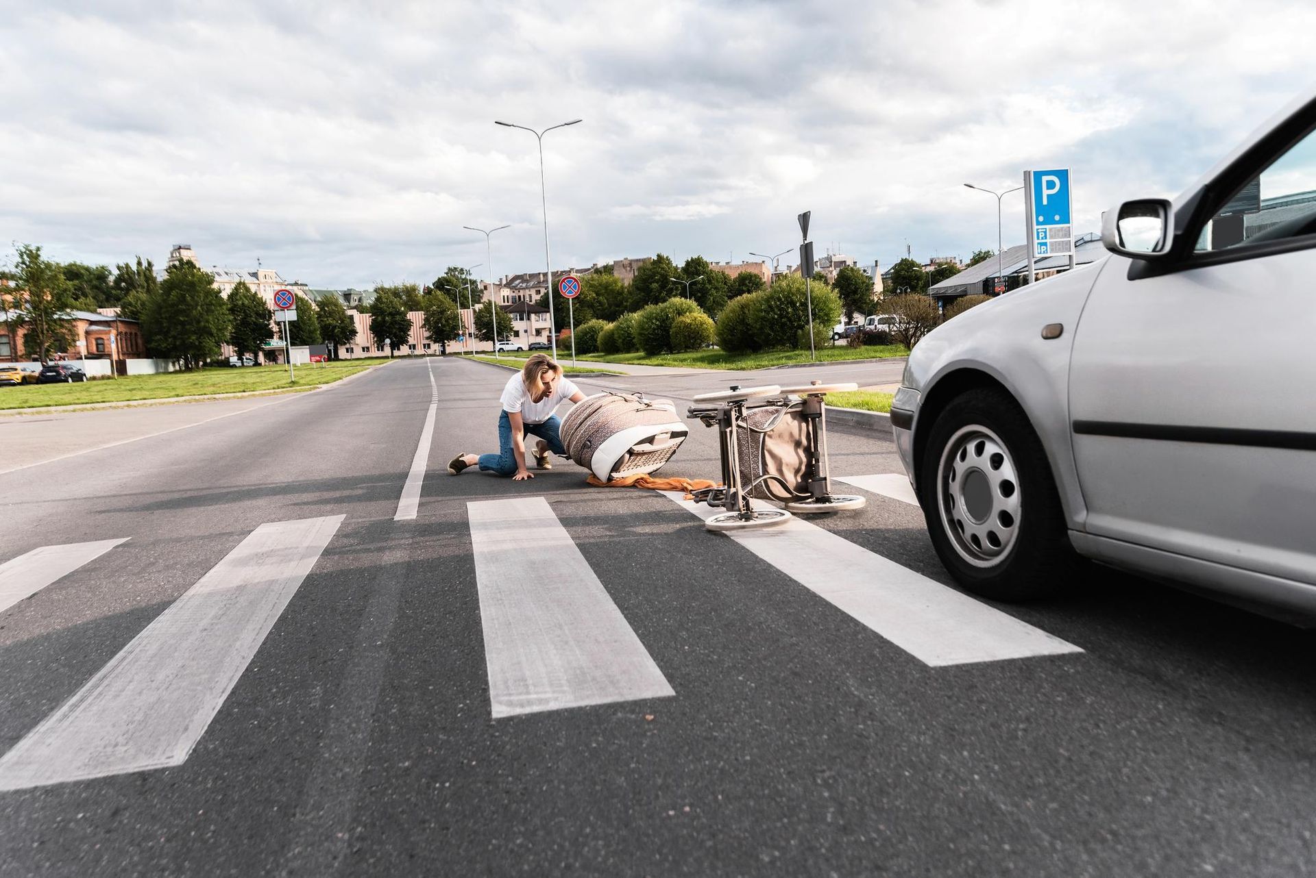 Person kneels beside a bicycle on a crosswalk near a silver car on a city street