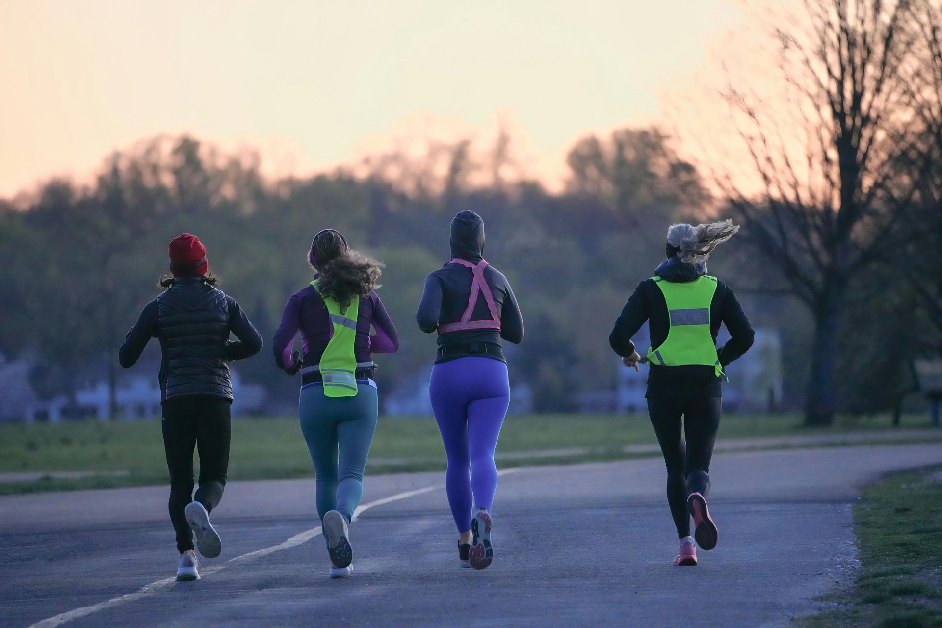 Four runners in reflective vests jogging along a park path at dusk