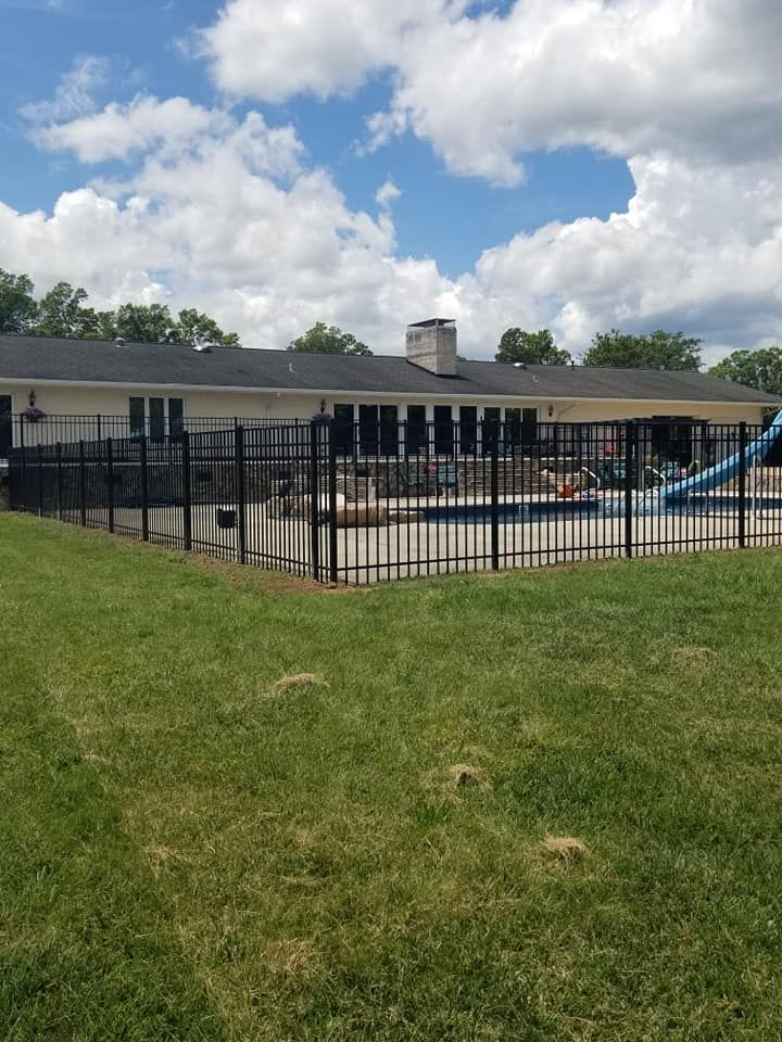 Outdoor pool beside a black fence and single-story building under a partly cloudy sky