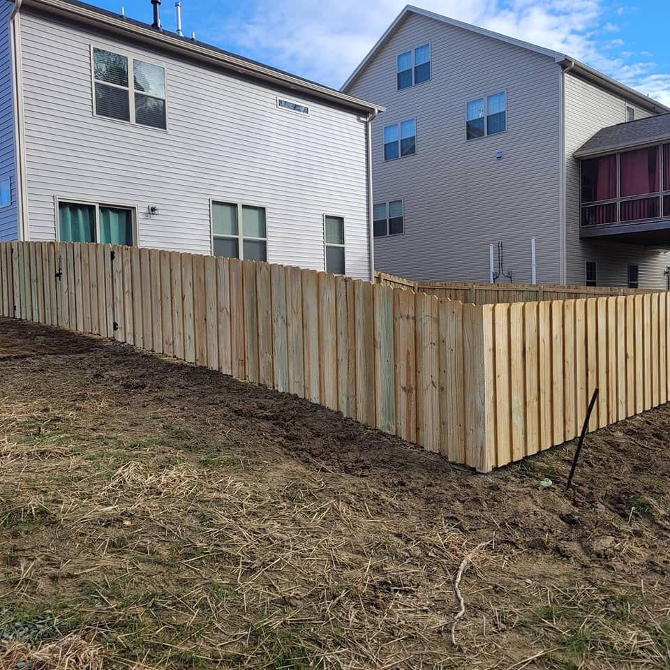 Wooden fence along a sloped dirt yard between residential houses on a cloudy day