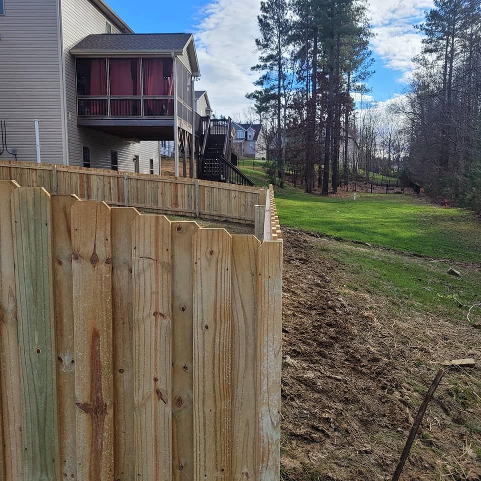 Wooden fence beside a house, with a grassy yard and trees under a partly cloudy sky.