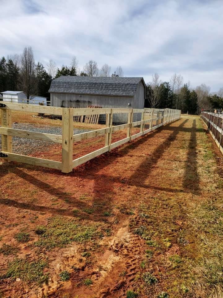 Wooden-fenced dirt path leading to a barn in a rural field under a cloudy sky
