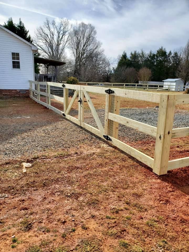Wooden fence with a gate beside a white house on a gravel and dirt yard under bare trees