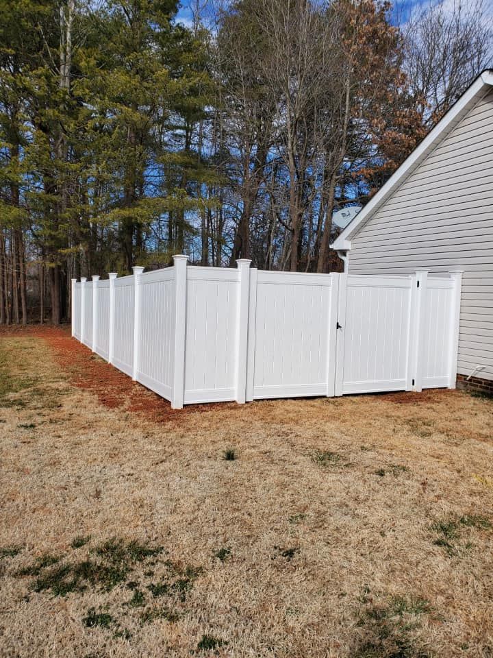 White vinyl privacy fence around a yard beside a house and trees