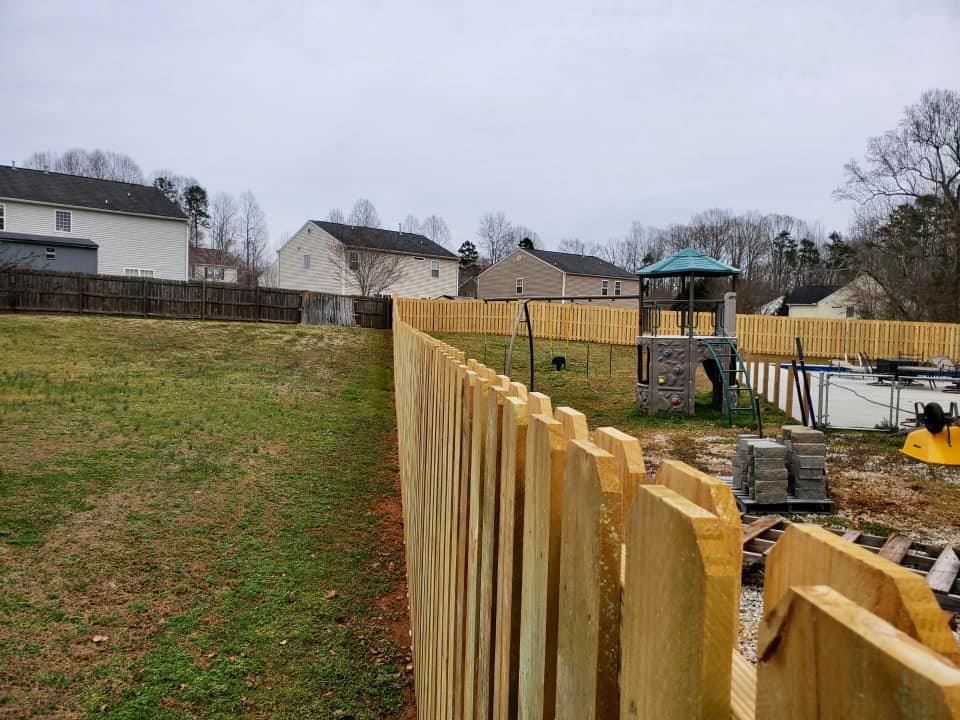Wooden fence bordering a grassy hillside near houses and a playground under a cloudy sky