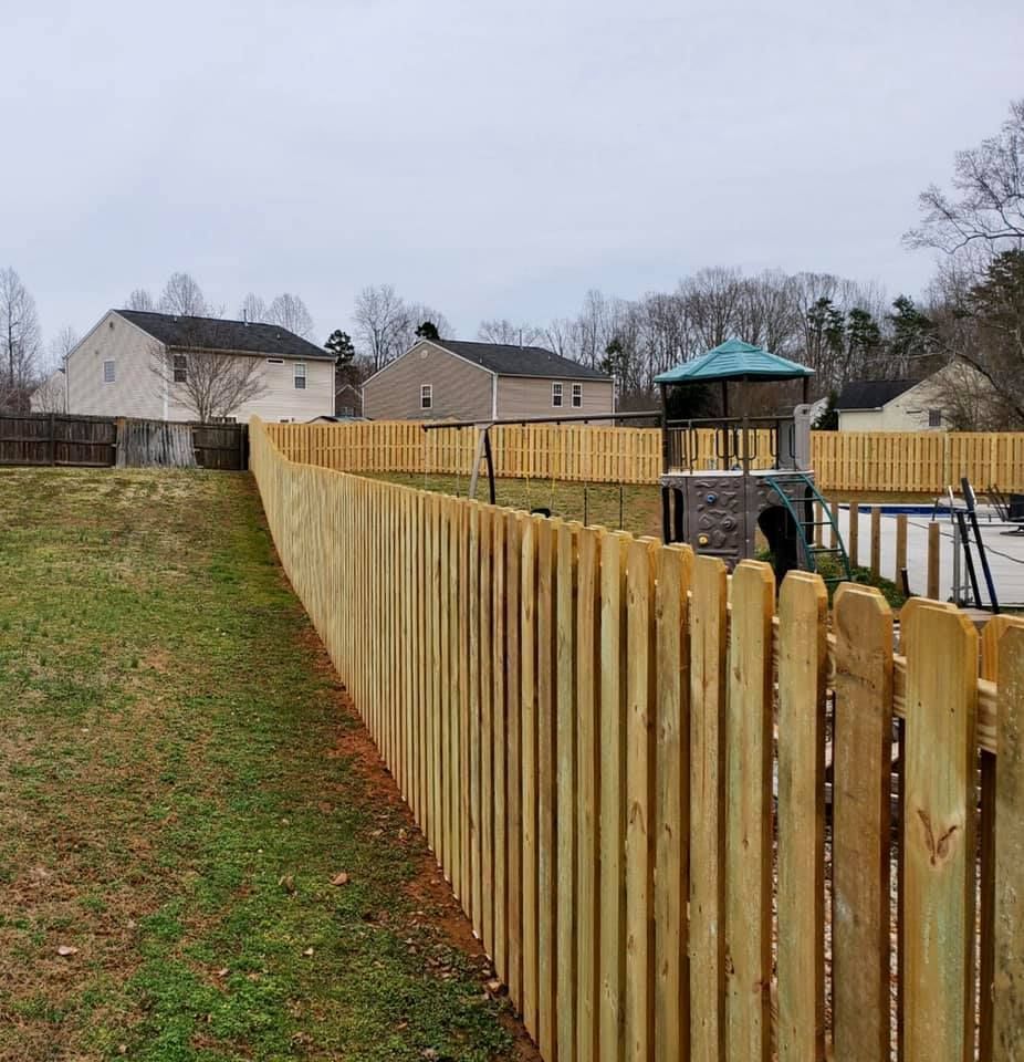 Wooden fence bordering a grassy yard with houses and a small playground under an overcast sky