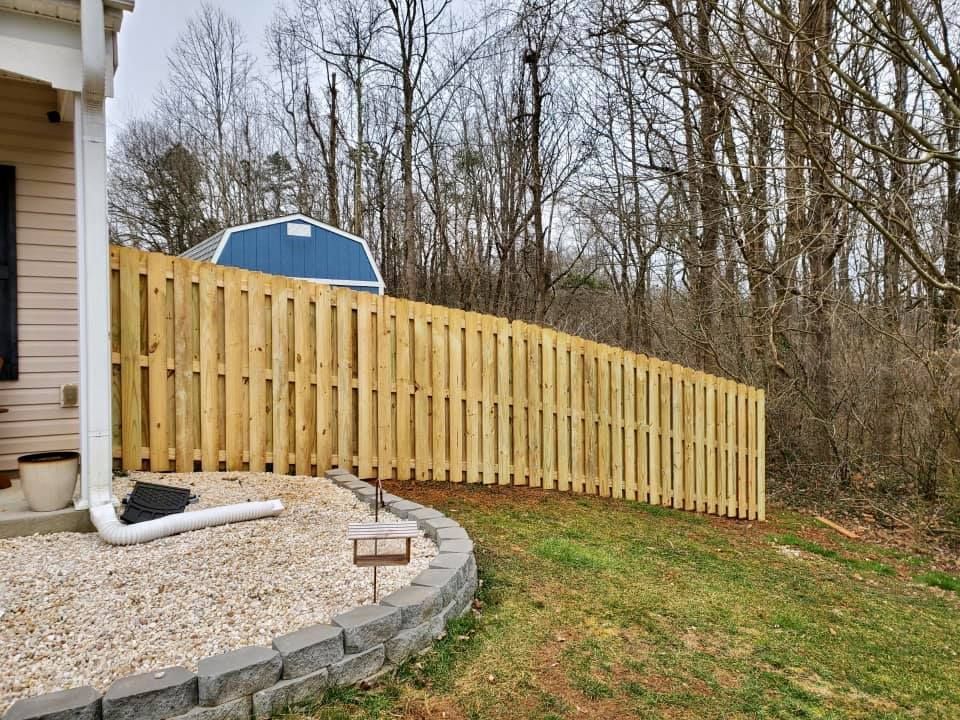 Freshly built tan wooden fence along a sloped yard beside a house and gravel patio
