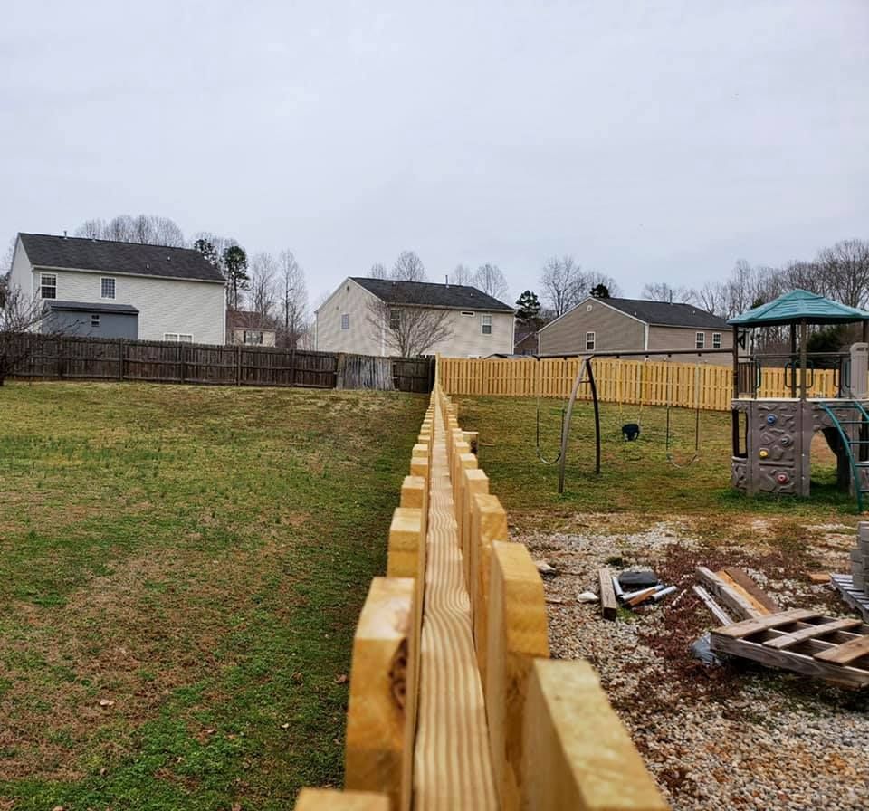 Wooden privacy fence running through a backyard with houses, grass, and a small play structure under cloudy skies