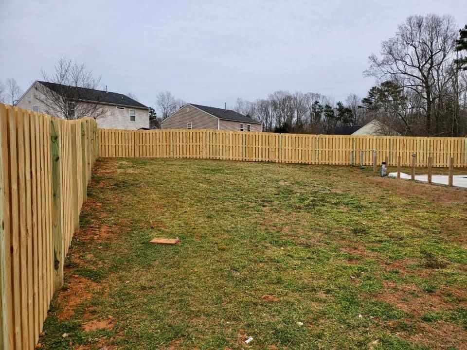 Grassy fenced backyard with a wooden privacy fence under a cloudy sky