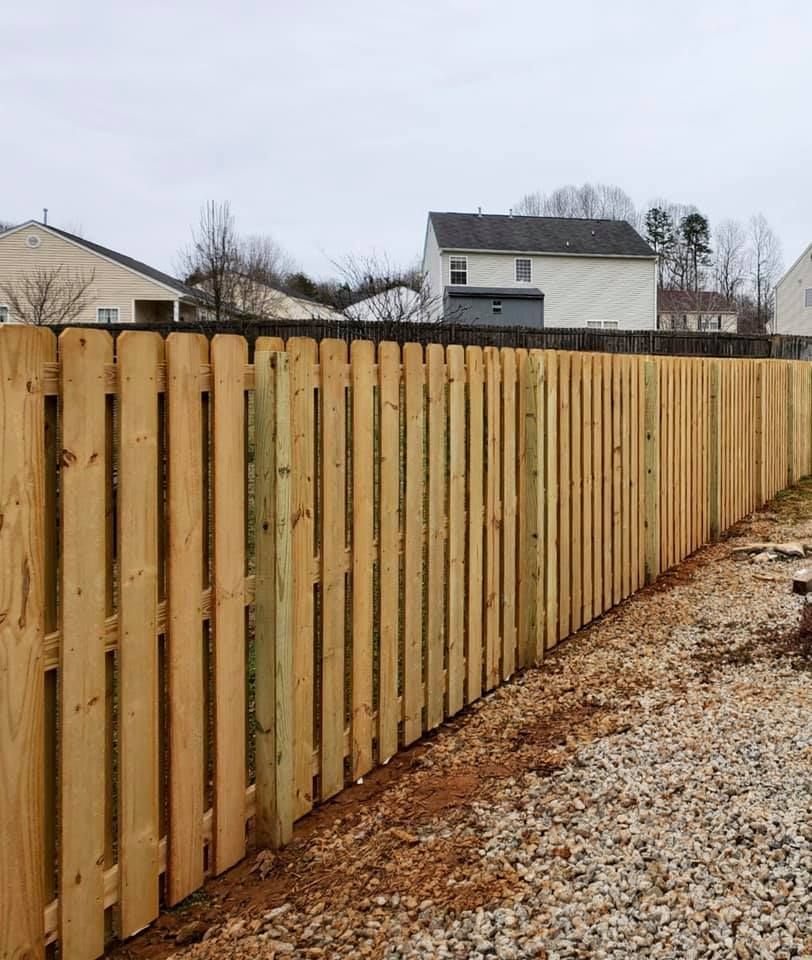 Long wooden privacy fence beside a gravel yard with houses in the background