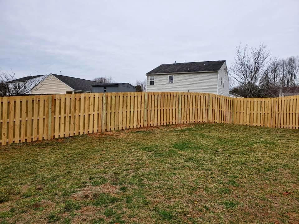 Wooden fence bordering a grassy yard with houses and leafless trees under an overcast sky