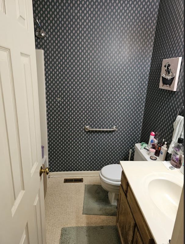 Small bathroom with a toilet, vanity sink, beige floor, and dark patterned wallpaper.