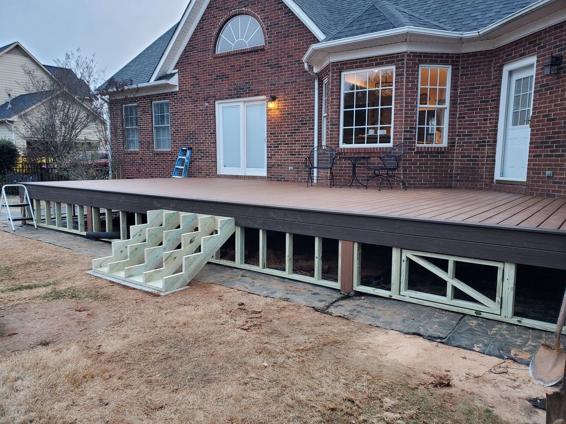 Brick house with raised wooden deck and small white stairs on a dirt yard