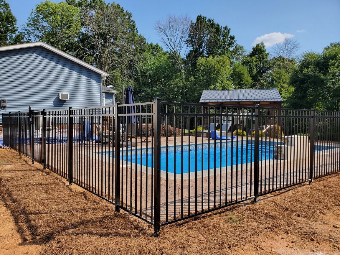 Black metal fence around a blue above-ground pool beside a house and trees in a backyard