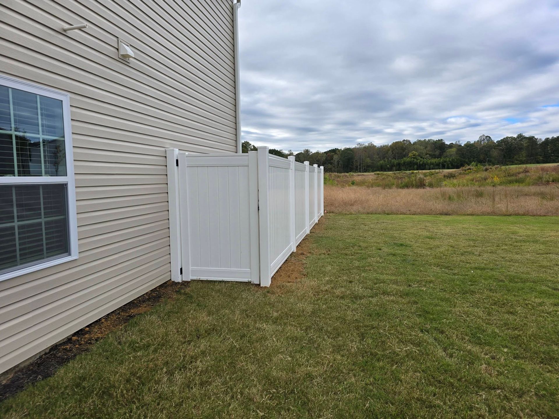 White fenced enclosure beside beige house in a grassy yard under a cloudy sky