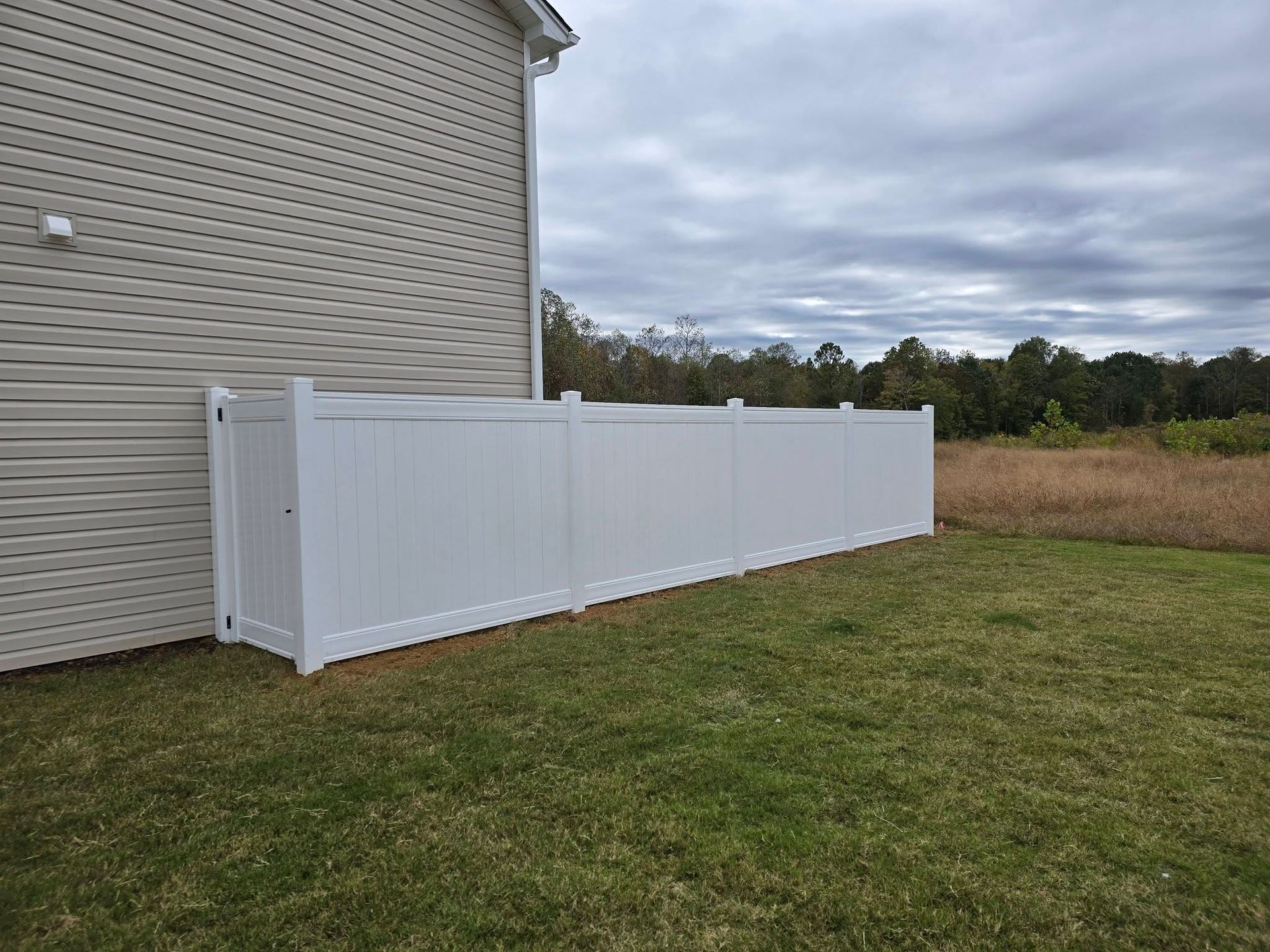 White vinyl fence along the side of a beige house beside a grassy yard