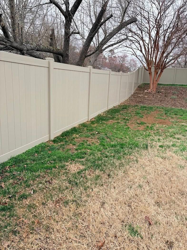 Backyard with a white fence, bare trees, patchy grass, and a leaf-covered slope