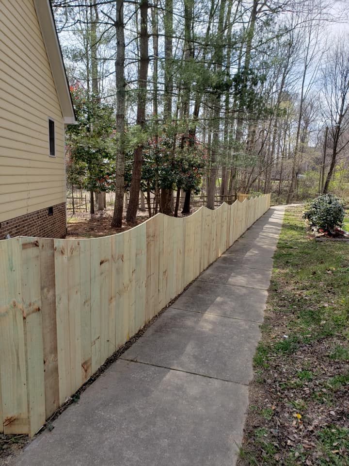 New wooden fence along a concrete sidewalk beside a house and wooded yard