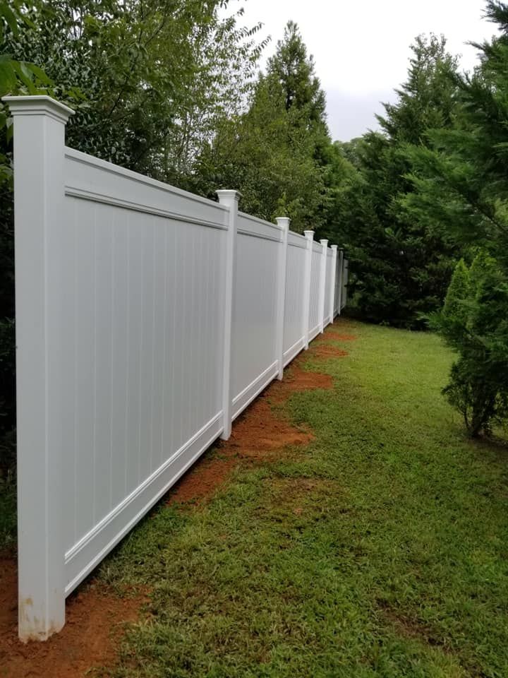 White vinyl fence along a grassy yard beside tall green trees