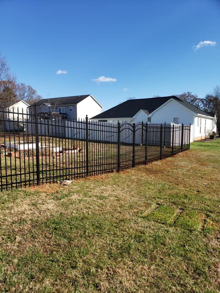 Black metal fence along a grassy yard with white houses under a blue sky.