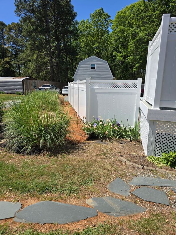 Backyard with white fence, small shed, stone path, and green plants under trees