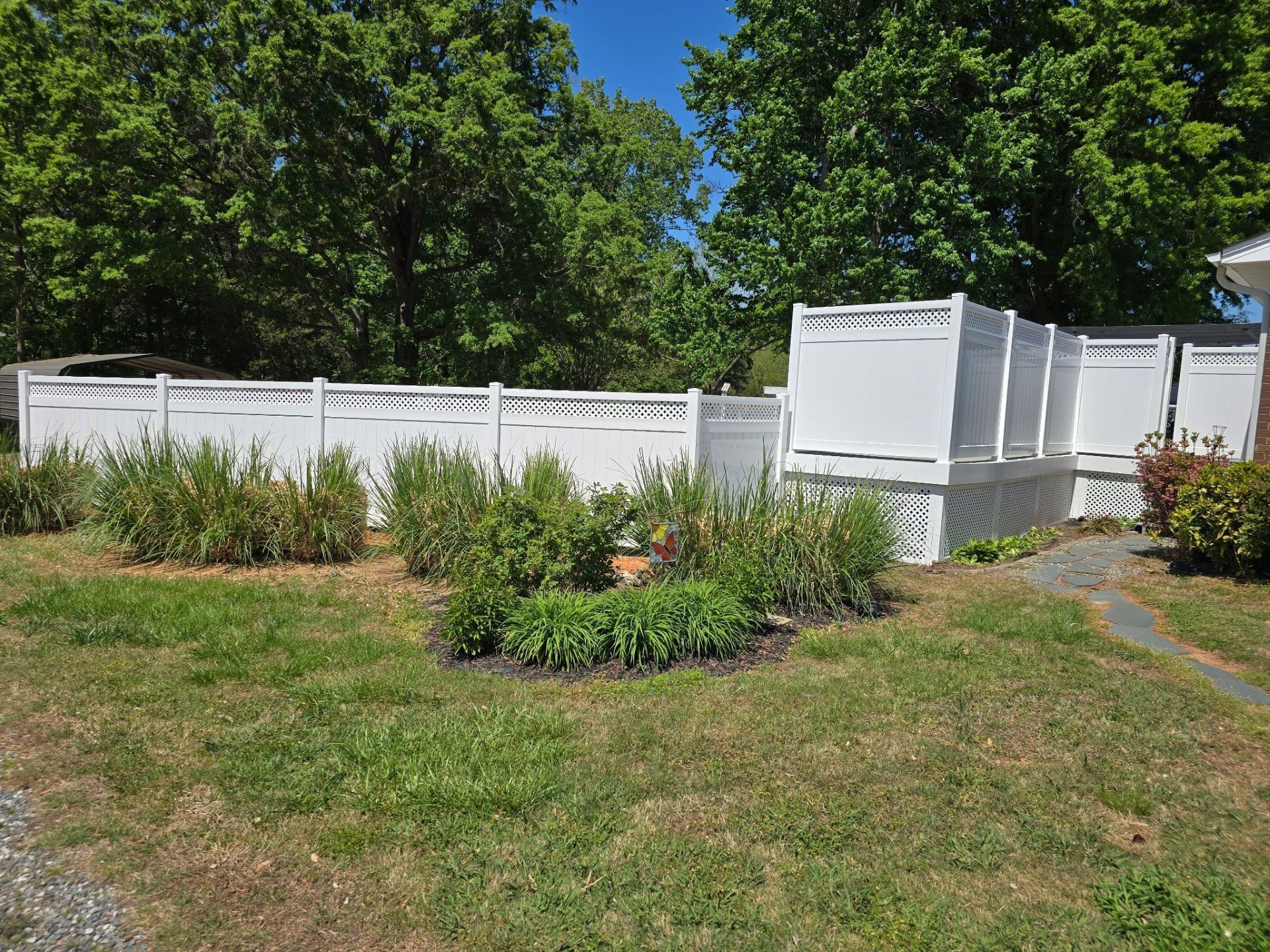 Backyard garden with white fence, raised beds, and green shrubs under trees