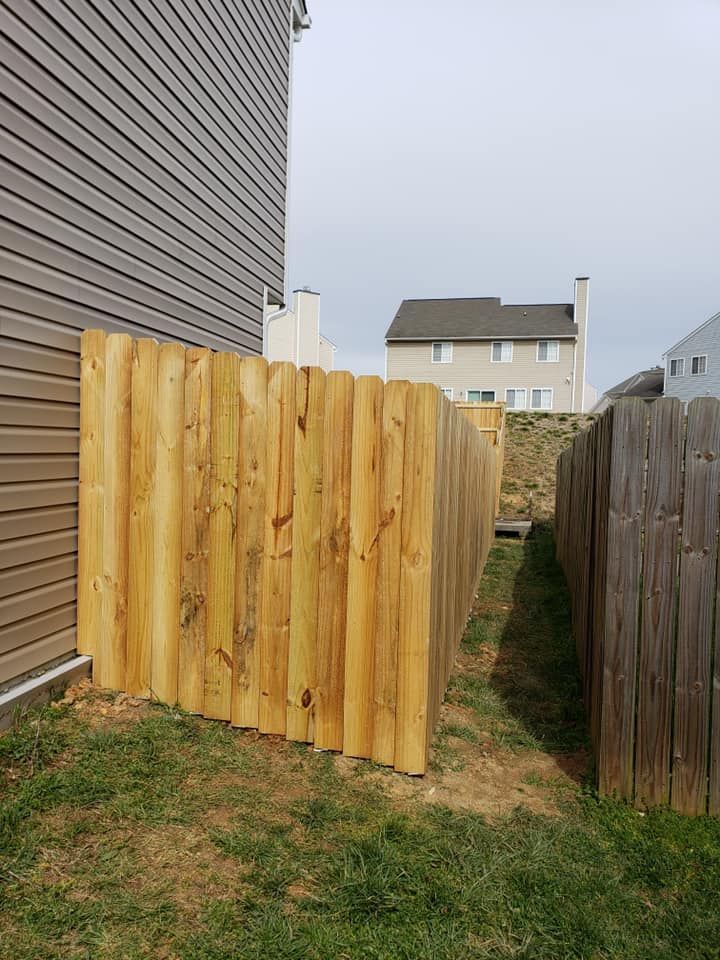 Freshly installed wooden fence panels between a house and a neighboring yard beside a narrow grass path