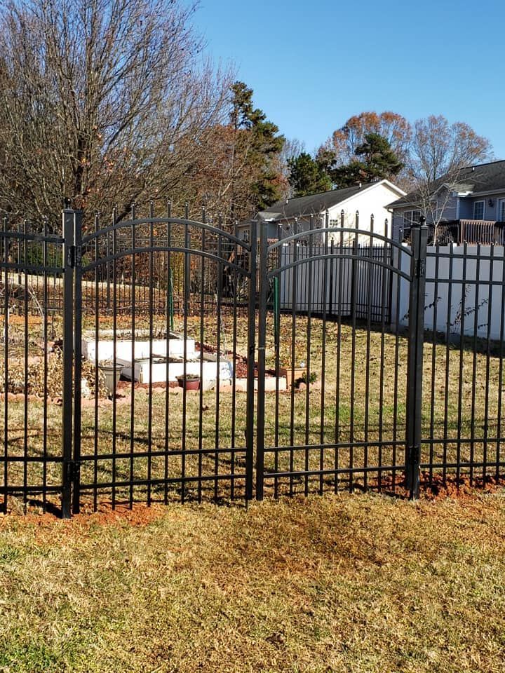 Black metal fence around a grassy backyard with a covered fire pit, trees, and houses in the background