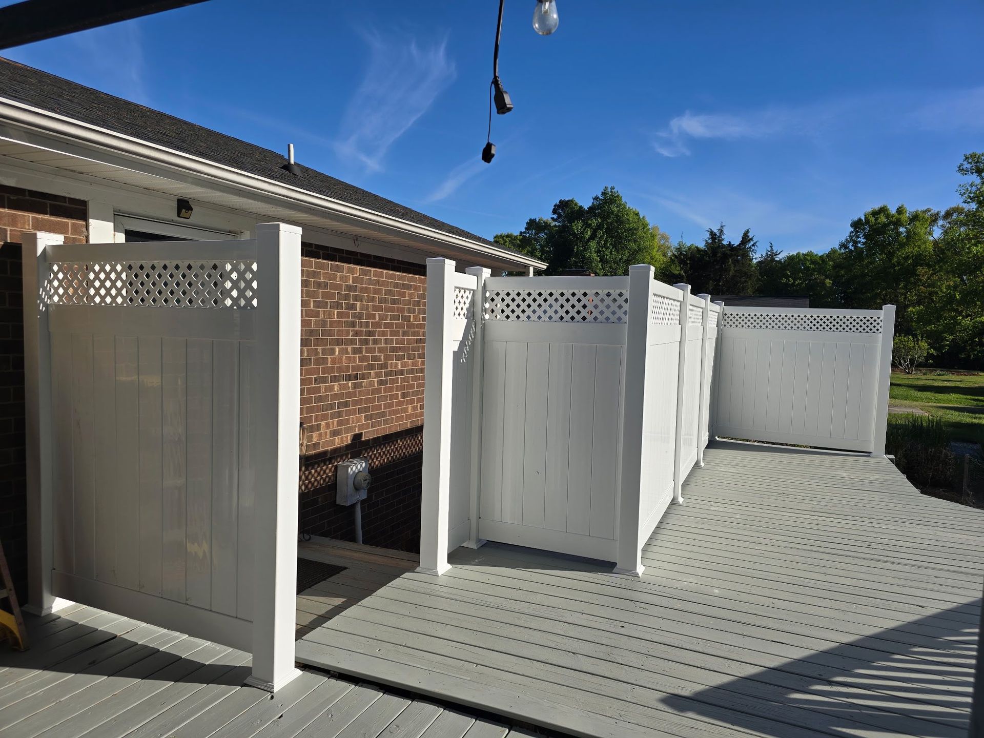 White outdoor privacy panels around a patio beside a brick house under a blue sky