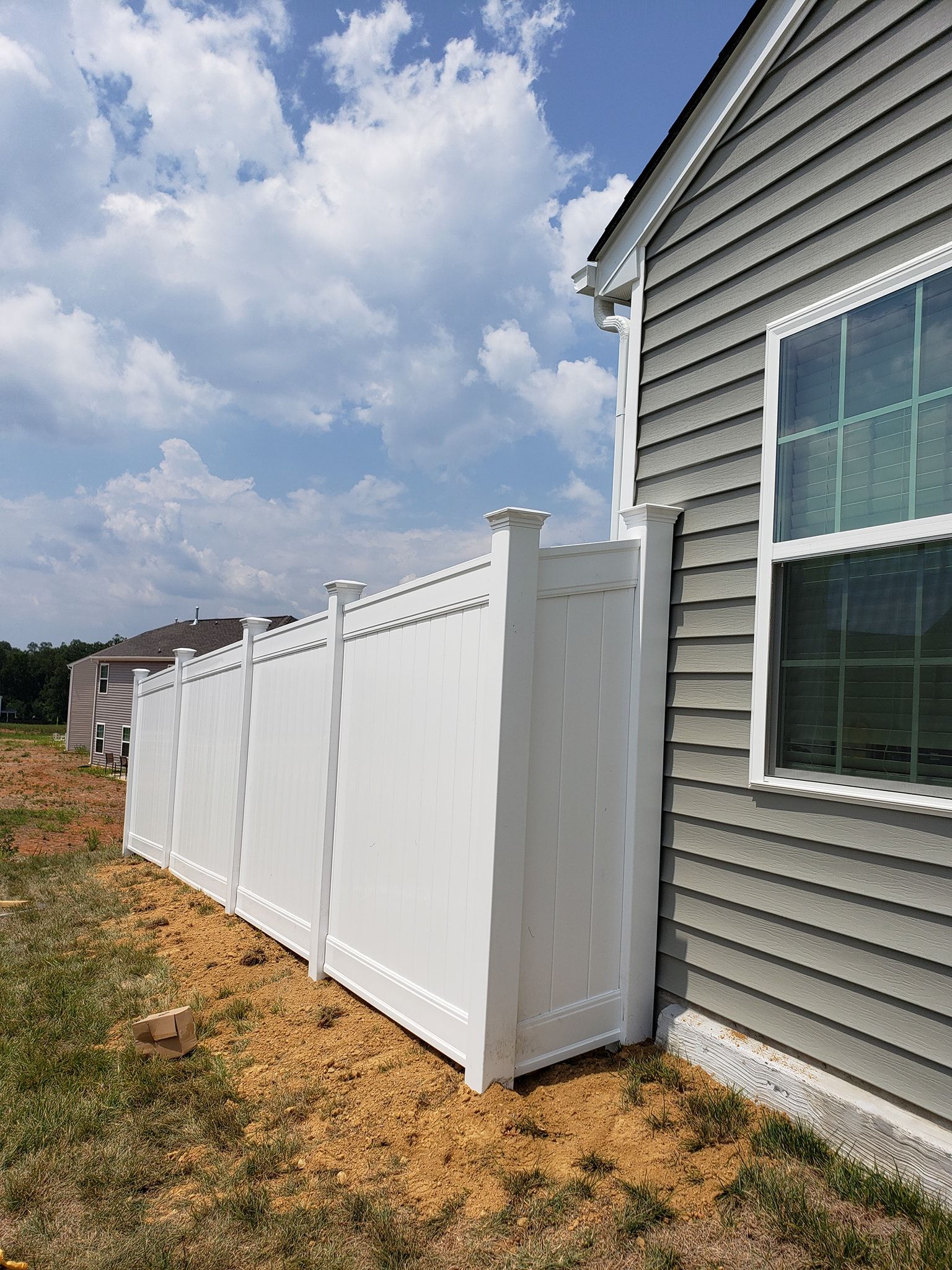 White vinyl fence along a gray house beside a window under a cloudy sky