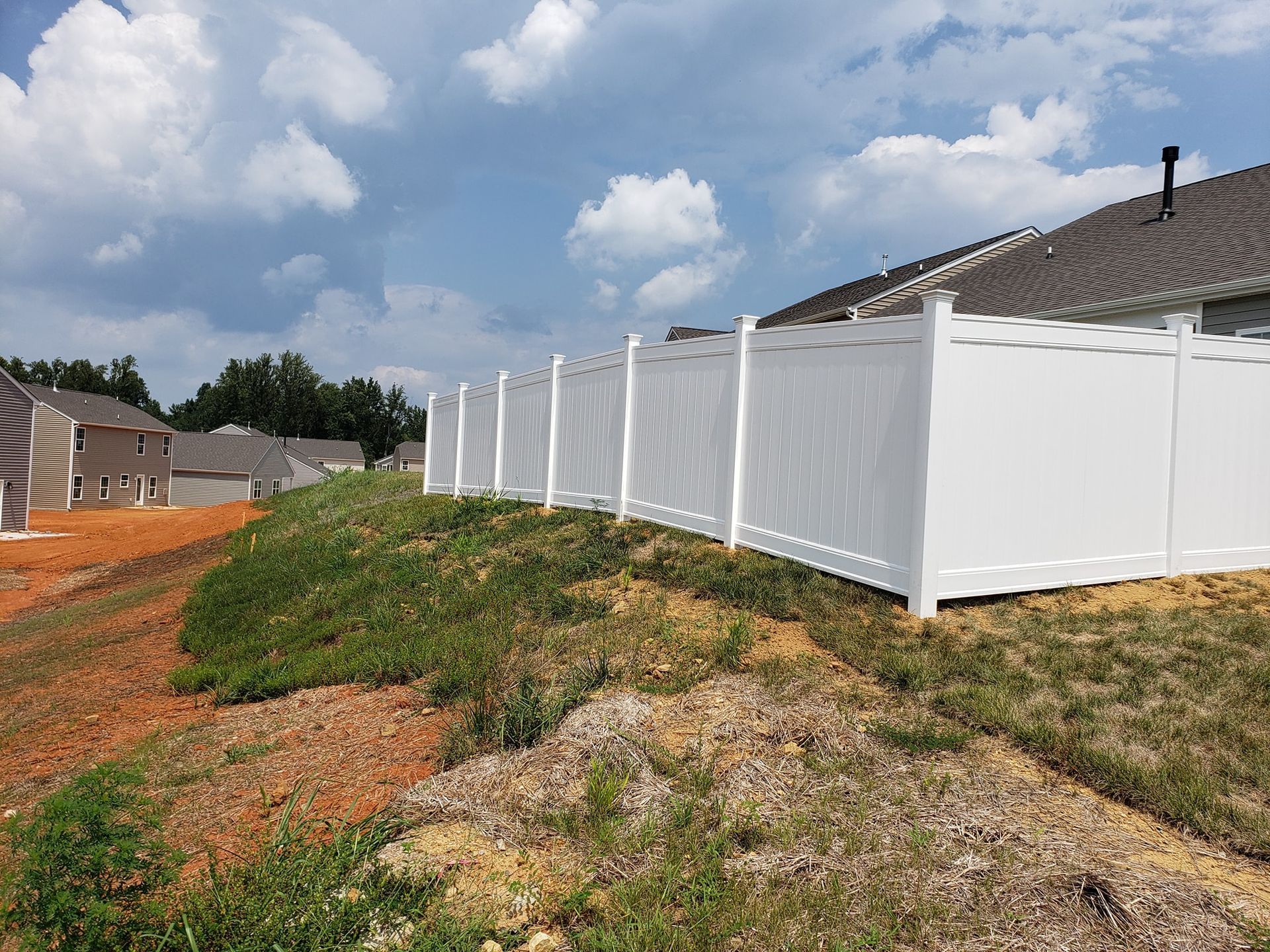 White privacy fence along a house on a grassy dirt lot under a cloudy sky