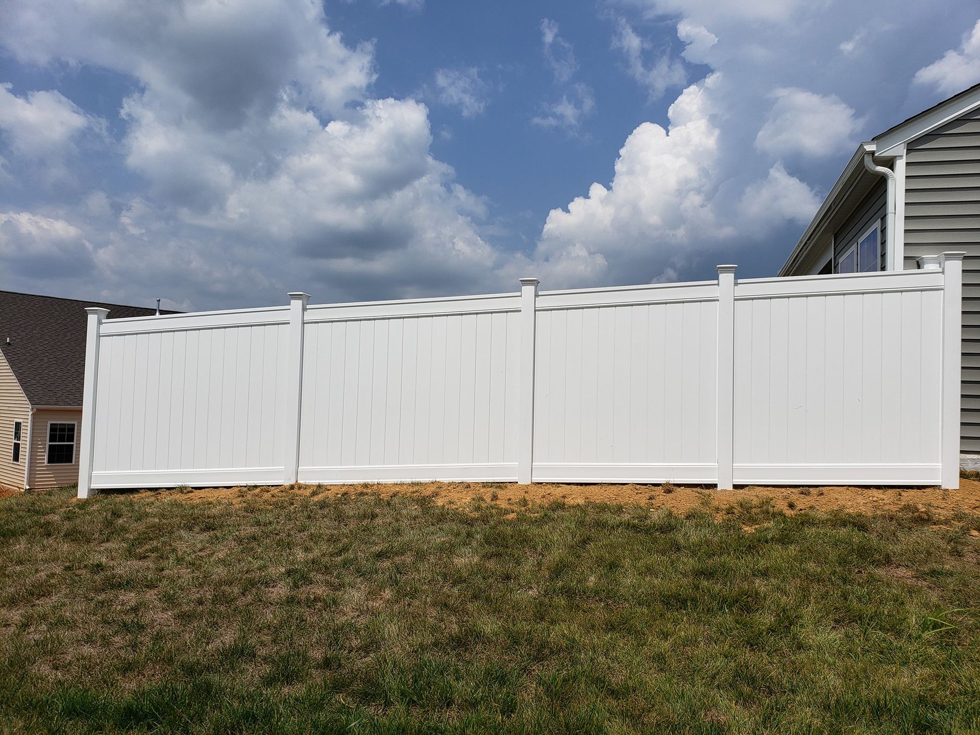 White vinyl privacy fence along a grassy yard under a partly cloudy sky