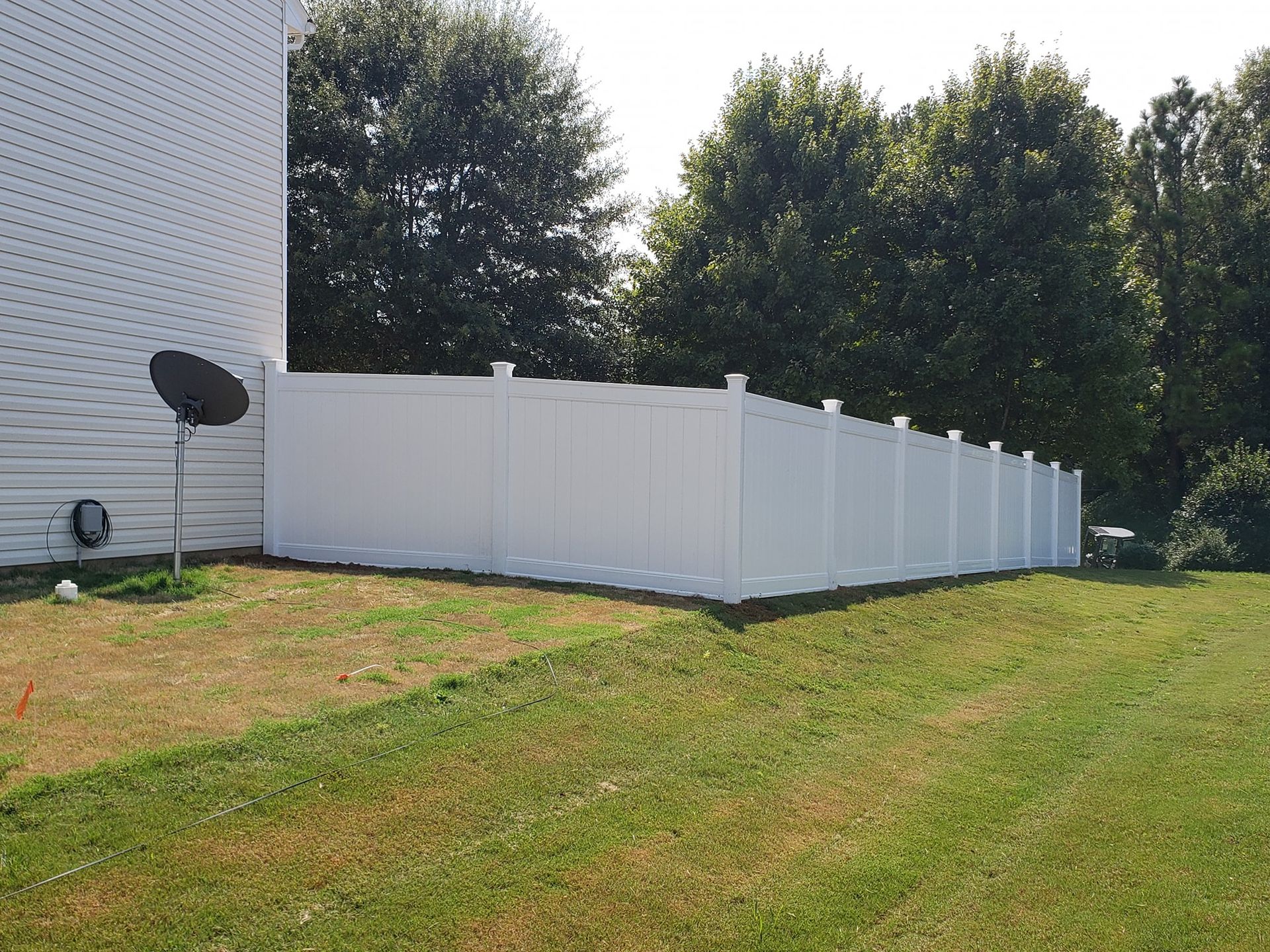 White vinyl fence along a grassy backyard beside a house and trees