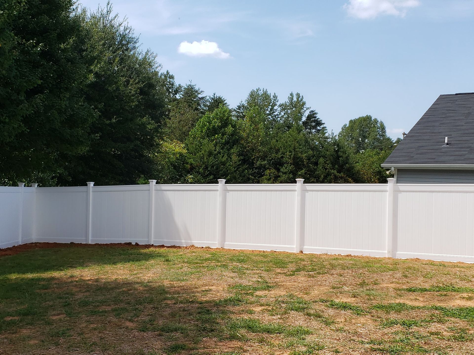 White vinyl fence bordering a grassy backyard with trees and a house roof under a blue sky