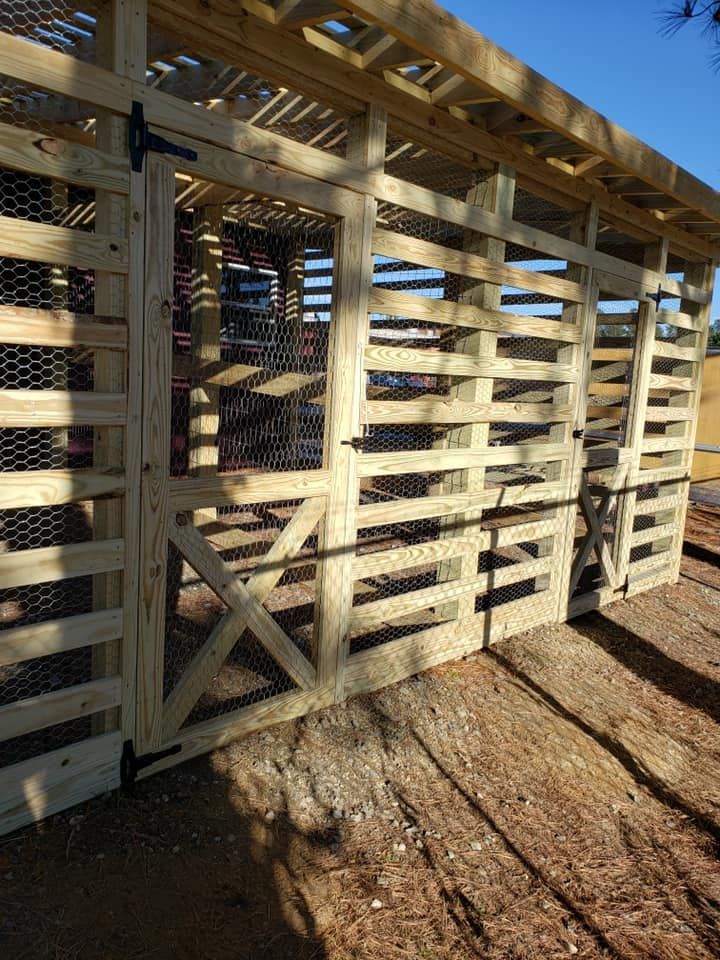 White wooden livestock pen under a roof with a slatted gate and dirt floor in sunlight
