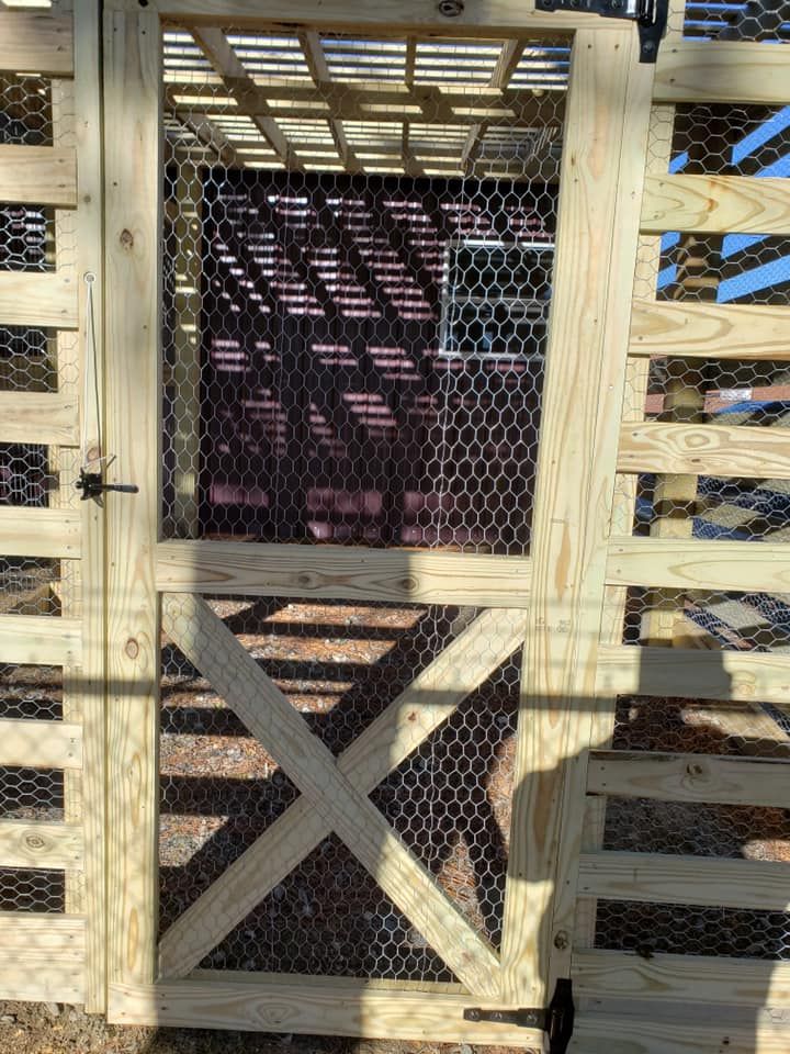 Wooden animal enclosure gate with wire mesh and cross-braced door in daylight