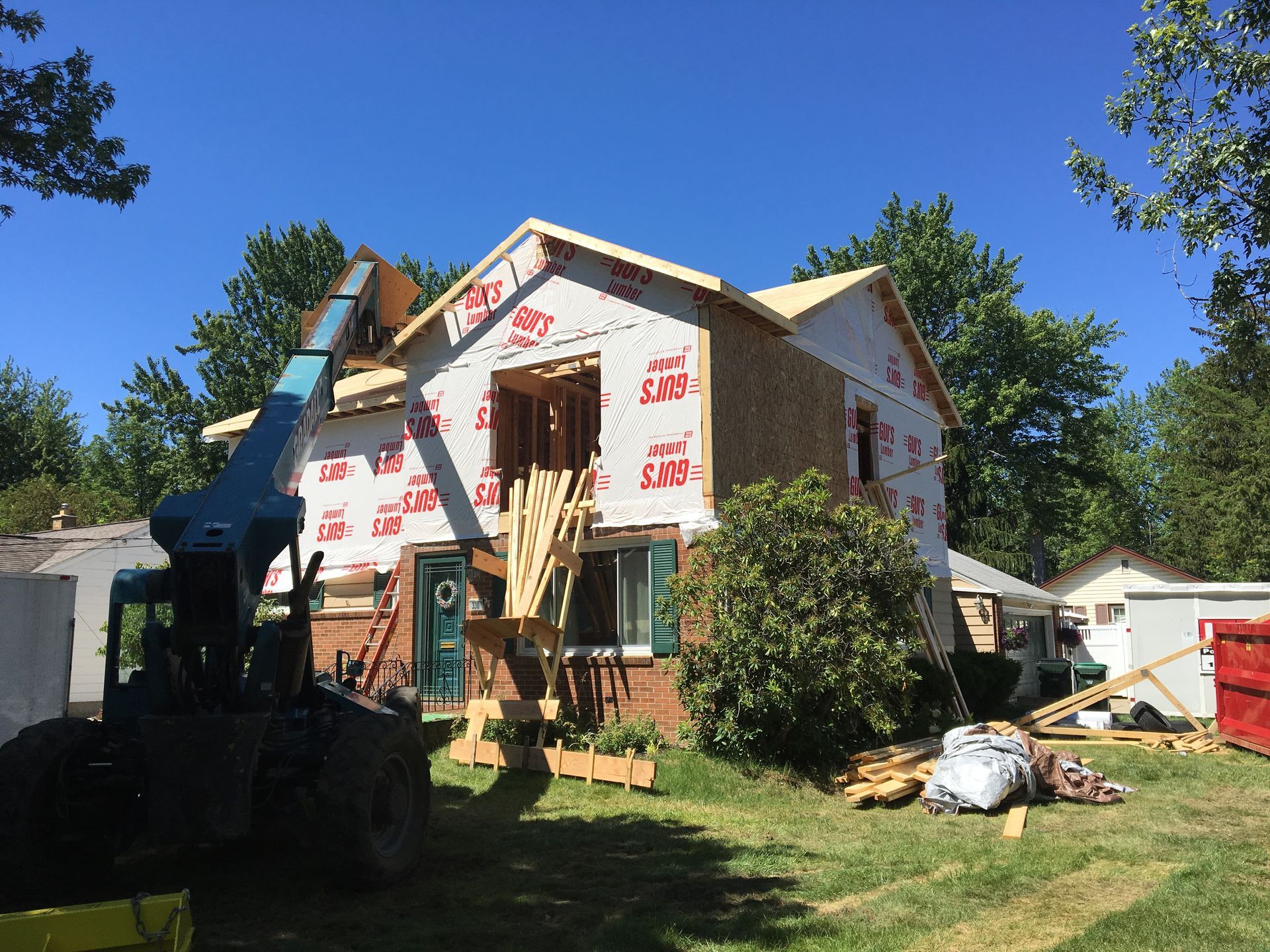 Straw-covered house under construction, with a porch, dormers, and chimney; set amongst trees.
