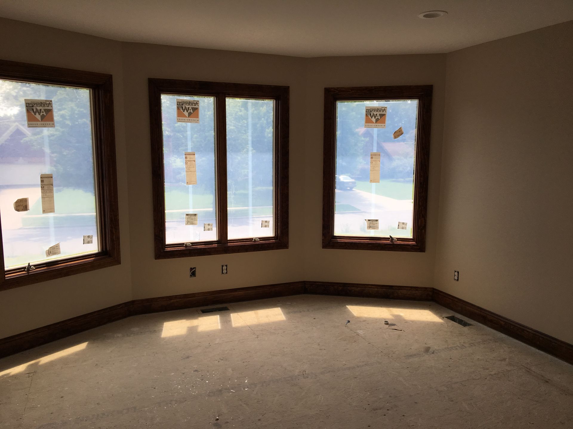 Wooden frame of a house under construction; blue sky, green trees surround.