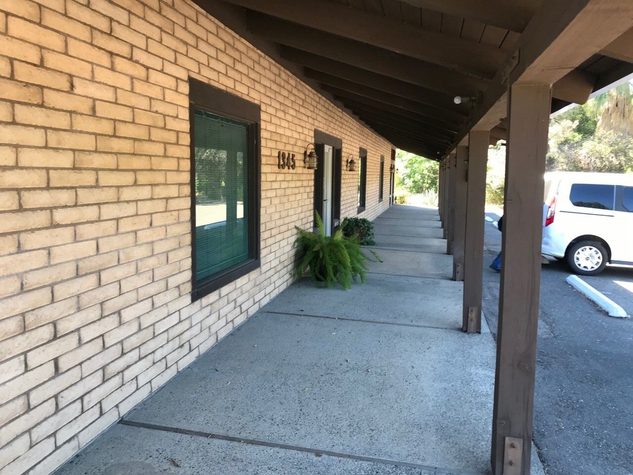 Covered sidewalk beside a brick building, with windows, wooden posts, and a parked white car.