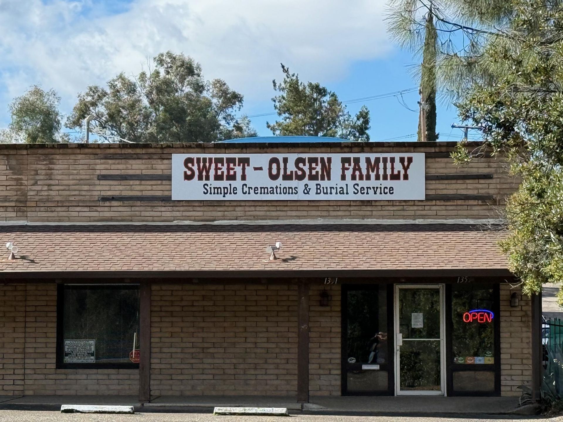 Storefront sign reading “Sweet Olsen Family” above a brick building with windows and an open door.