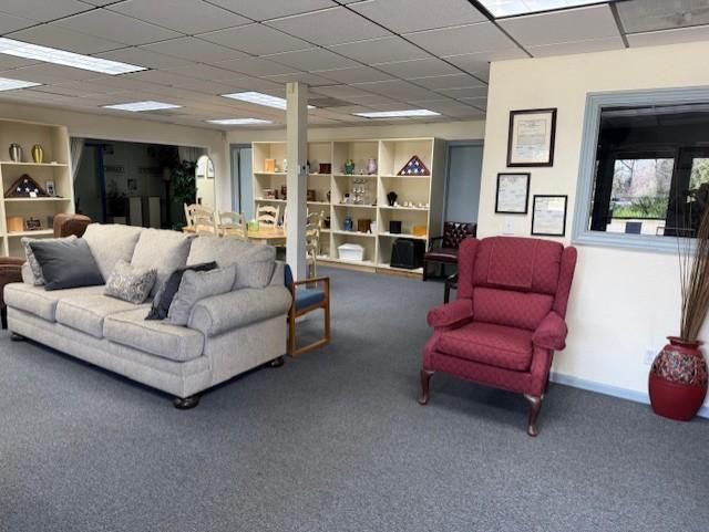 Carpeted living room with gray sofa, red armchair, shelves, and window in a bright office-like space