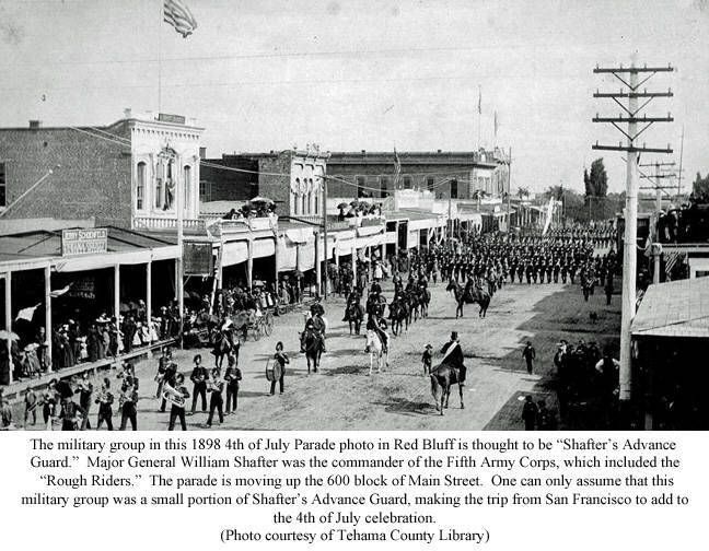 Parade of marching soldiers along a city street lined with storefronts and spectators, black-and-white photo