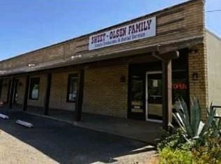 Small brick storefront with a sign reading “... Family,” shaded sidewalk, and desert plant in front.