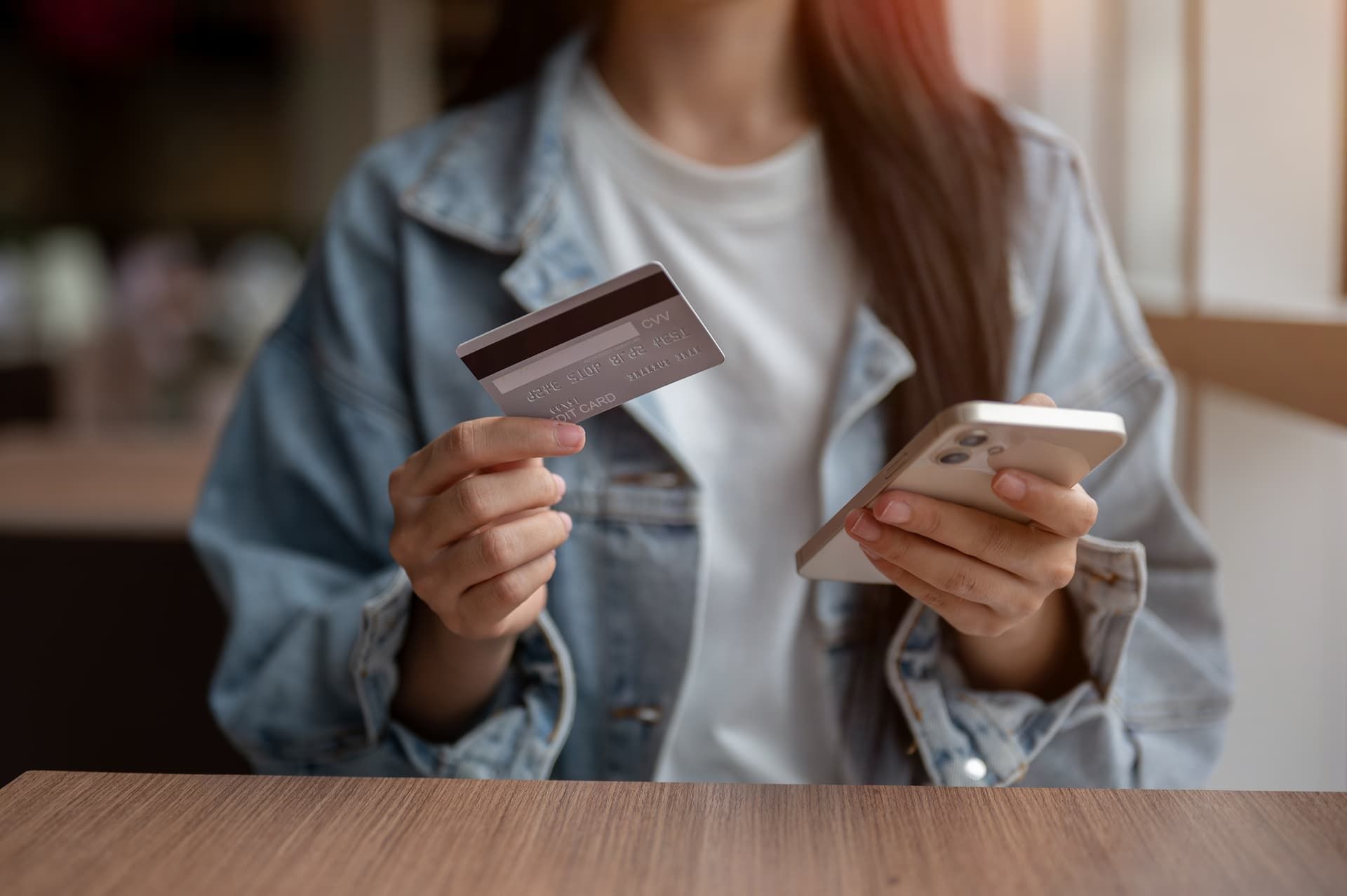 Person holding a credit card and smartphone at a table, suggesting an online purchase